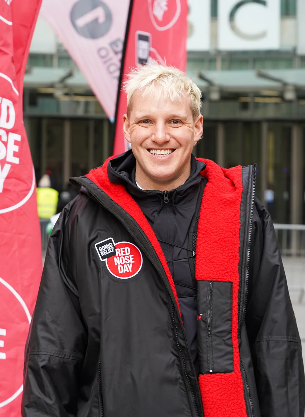 Person wearing a dryrobe with a 'Red Nose Day' logo, standing in front of banners