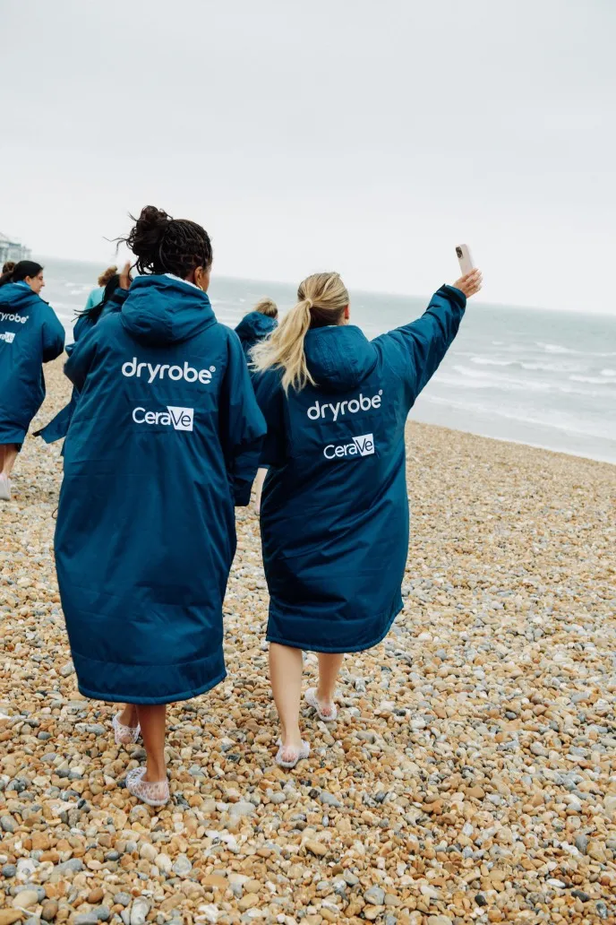 People wearing blue dryrobe-Cerave on a pebbly beach.
