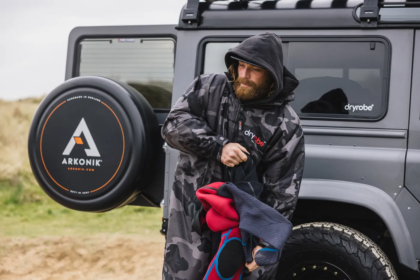 A surfer putting his wetsuit the right way while wearing a black camo Dryrobe